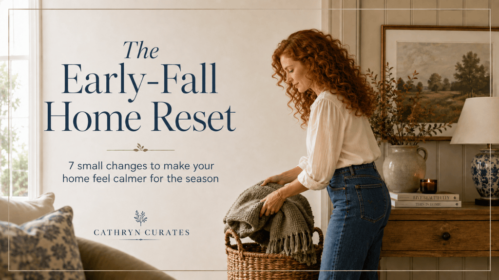 A slender curly-haired redhead folds an olive-green throw into a woven basket in a bright, softly styled living room with warm wood furniture, autumn branches, heritage-blue accents, and subtle fall decor. Text reads “The Early-Fall Home Reset: 7 small changes to make your home feel calmer for the season.”
